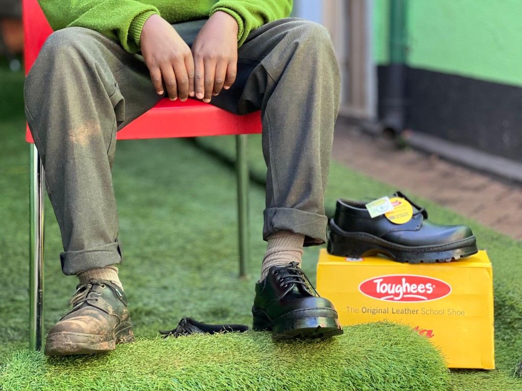 Learner showing worn shoes beside new Toughees school shoes from Hive support